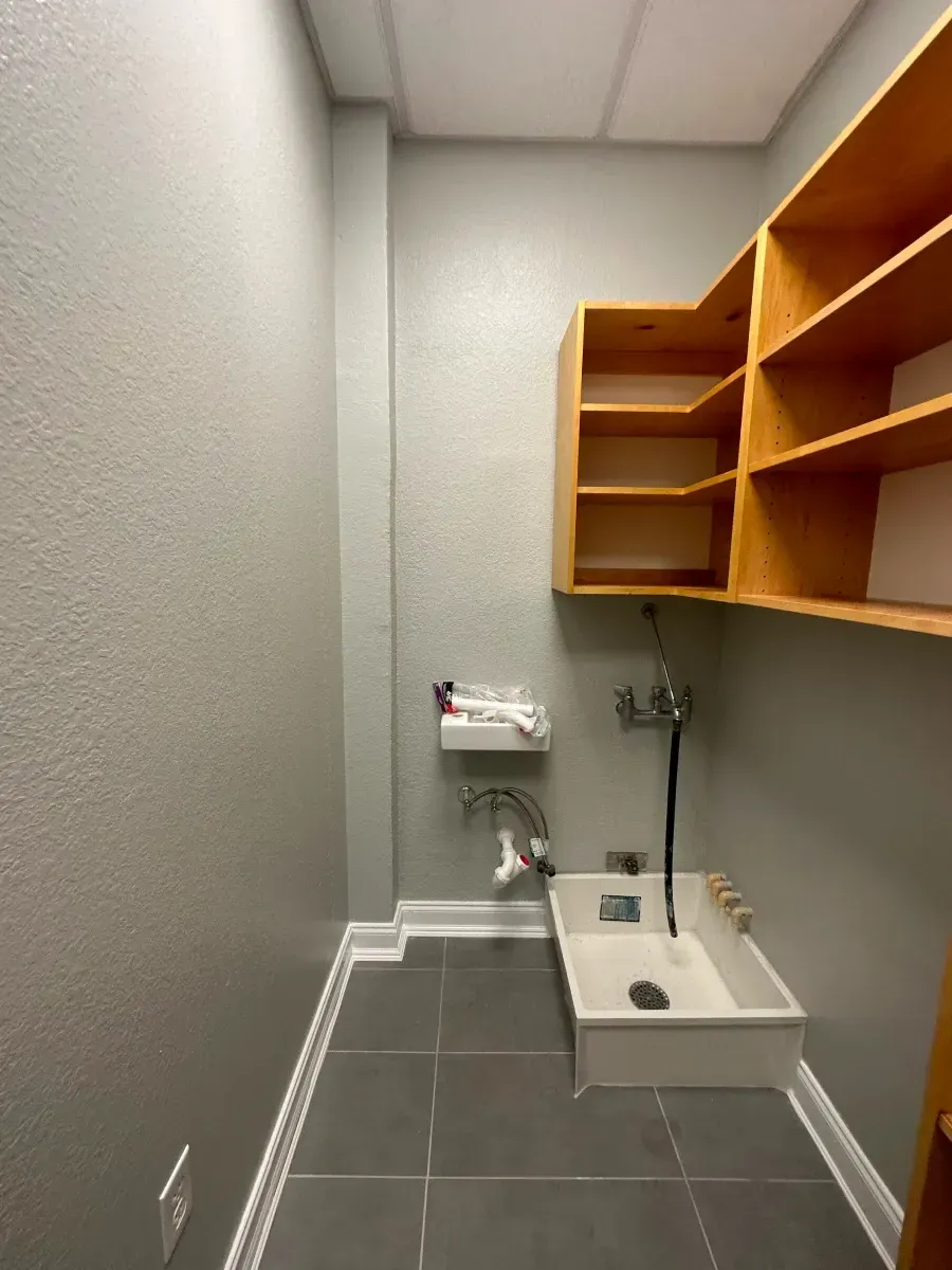Laundry room with a utility sink, gray walls, tile floor, and wooden shelves.