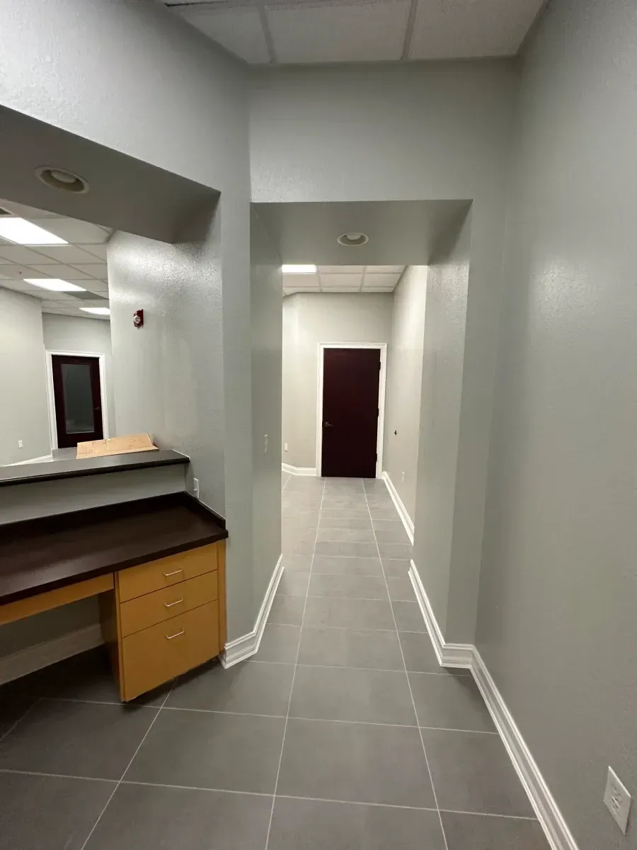 Narrow office hallway with gray walls, tiled floor, and a desk on the left.
