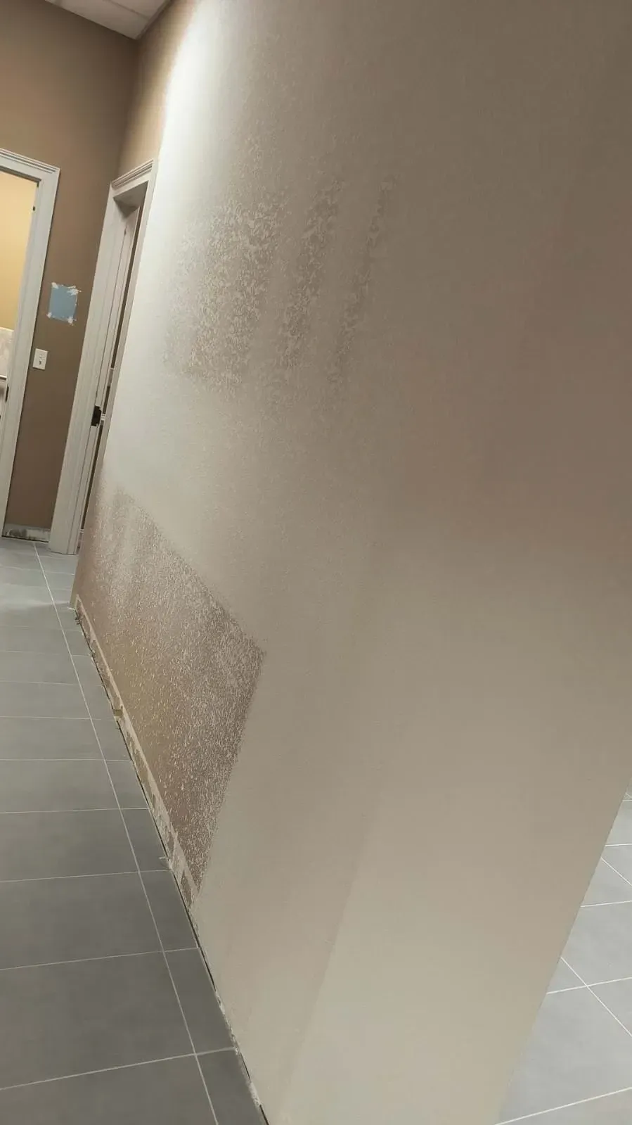 Beige hallway with textured wall sections, gray tile floor, and open doorway.