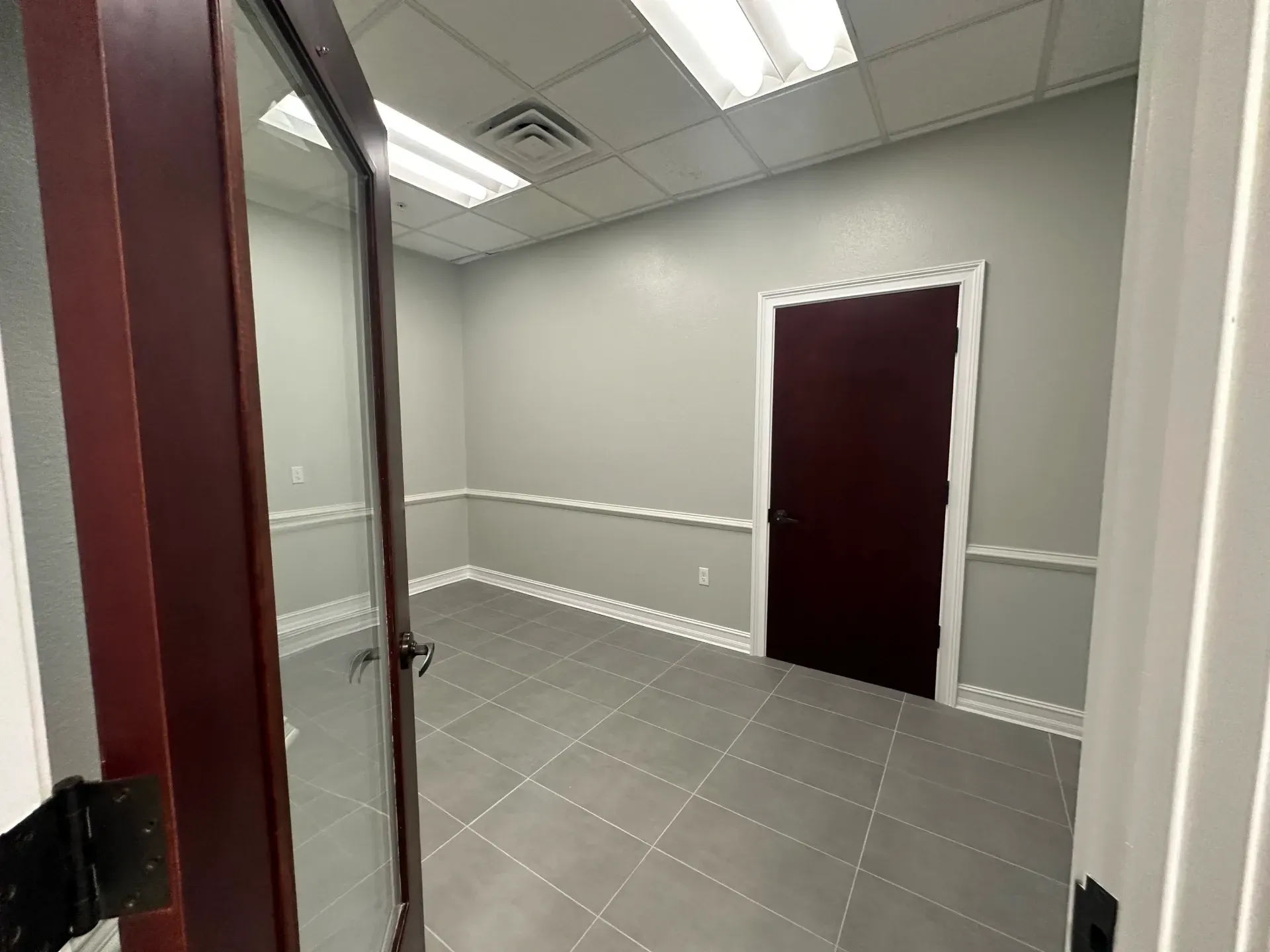 Empty office space with gray tile floor, gray walls, and a burgundy door.