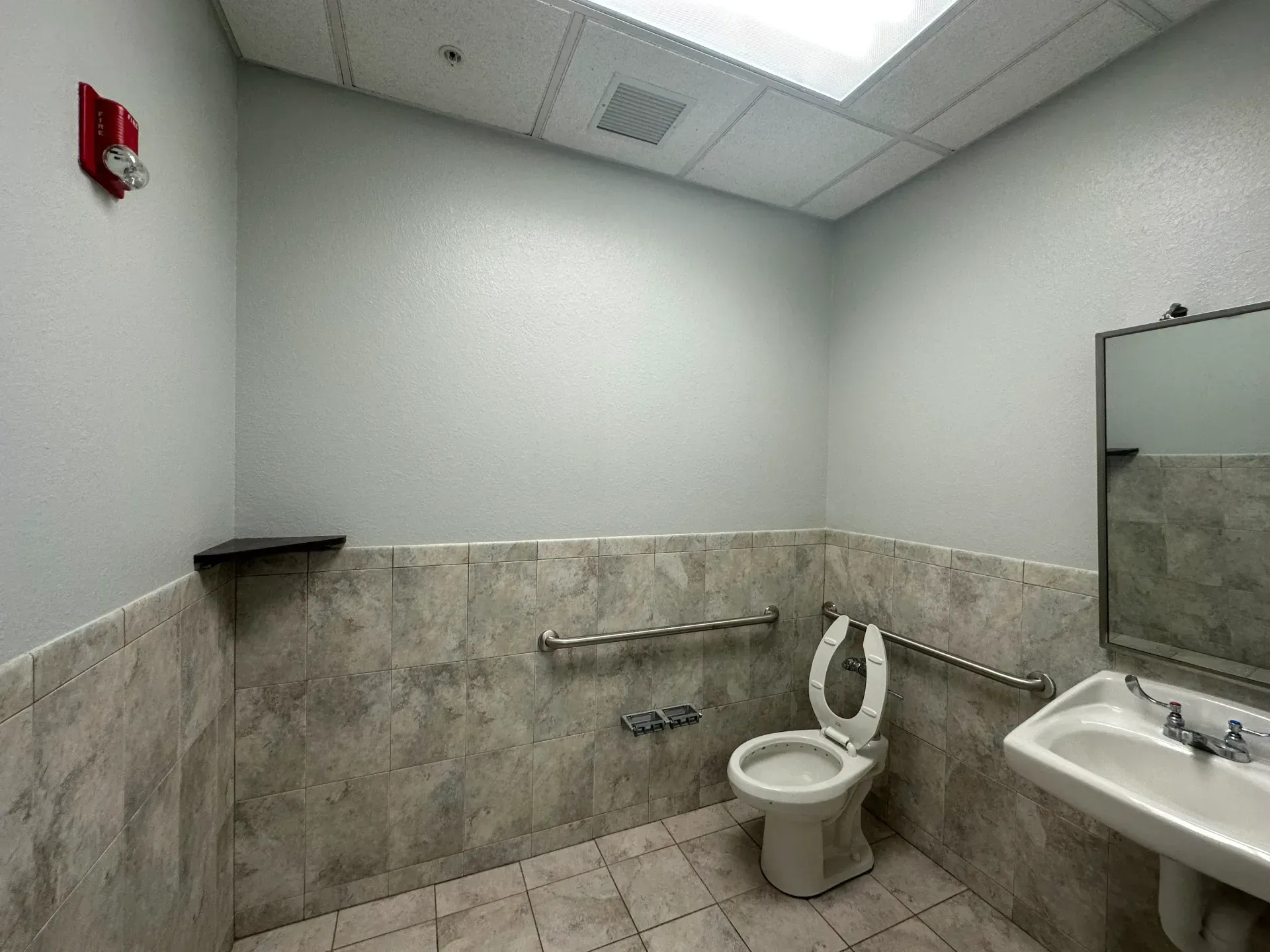 ADA accessible restroom with toilet, sink, grab bars, and fire alarm.