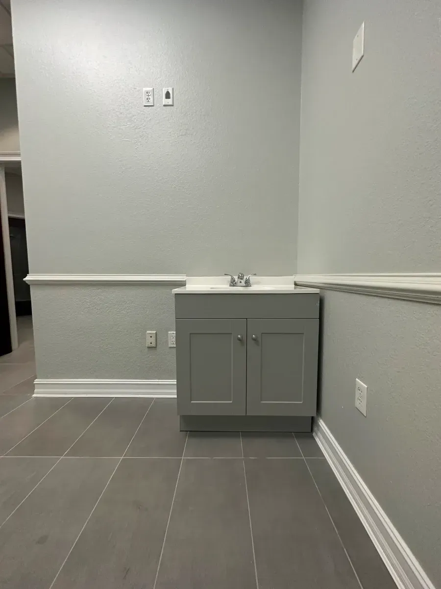 Gray bathroom vanity against gray walls, white trim, and gray tile floor.