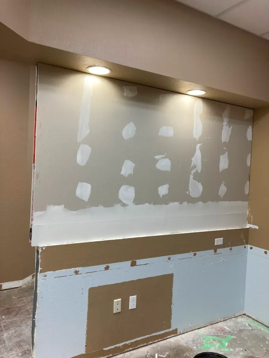 Interior wall under construction with recessed lighting; drywall and mudding visible.