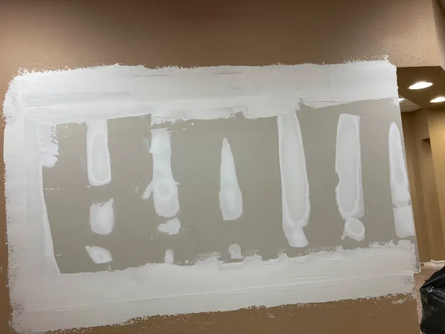 Rectangular area of drywall repair; white mud applied to the edges and in vertical strips. Brown wall.