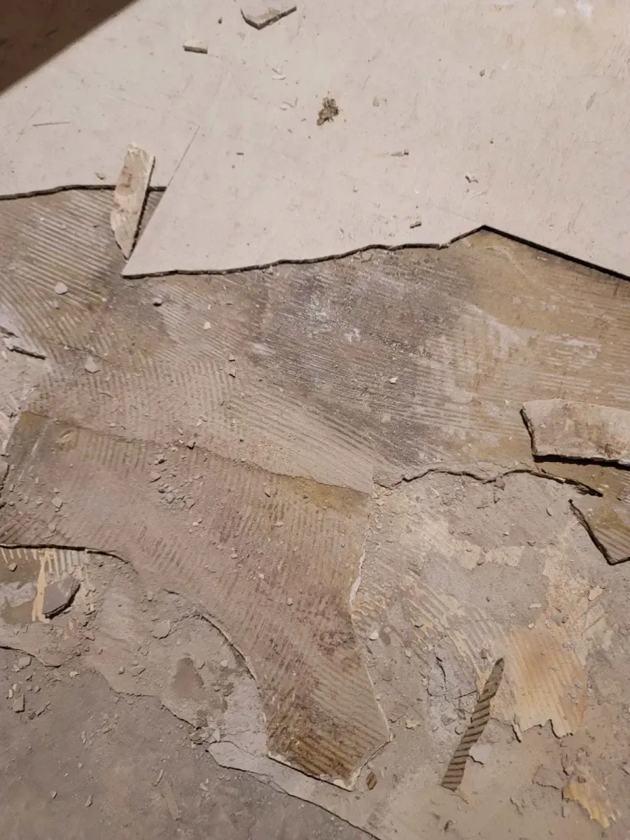 Floor with remnants of tile and adhesive, showing areas of bare subfloor and torn pieces.
