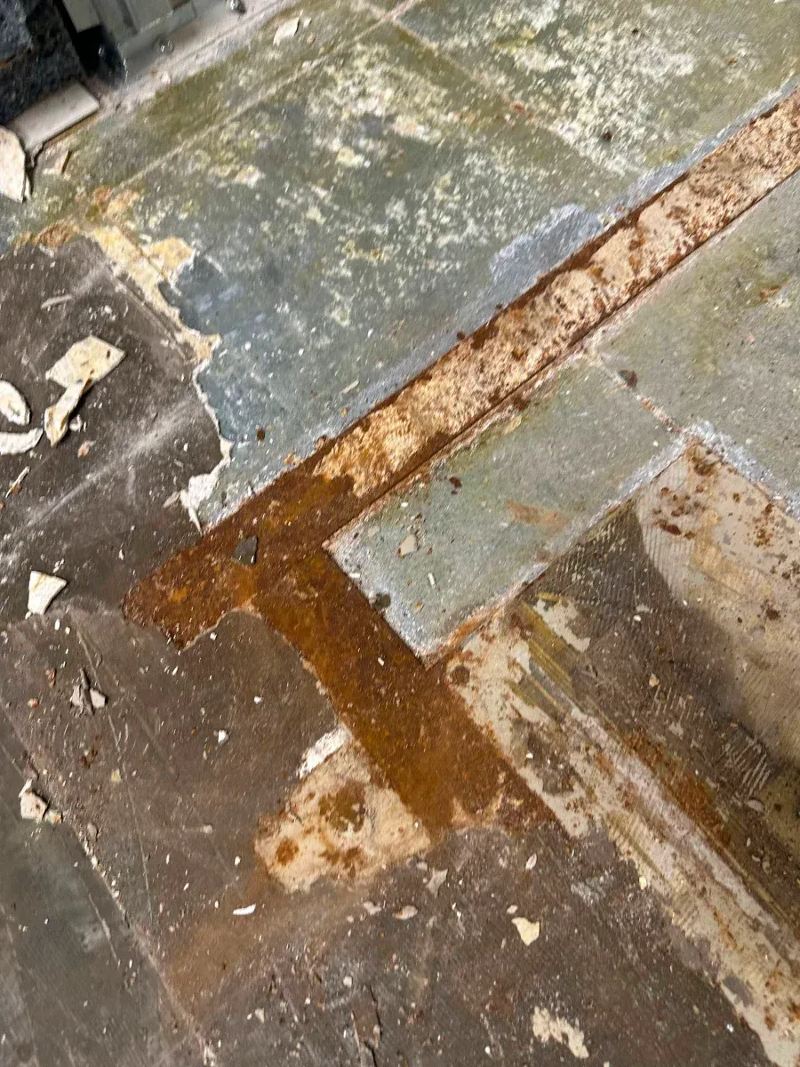 Close-up of a deteriorating floor with a rusty, rectangular design. Gray and brown colors dominate the scene.