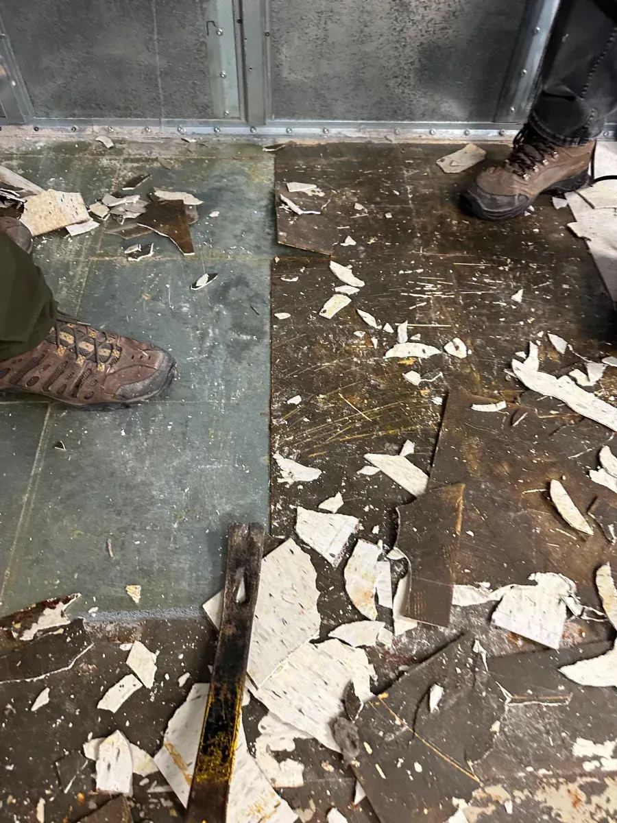 Feet standing on a partially demolished floor, with scattered tile fragments.
