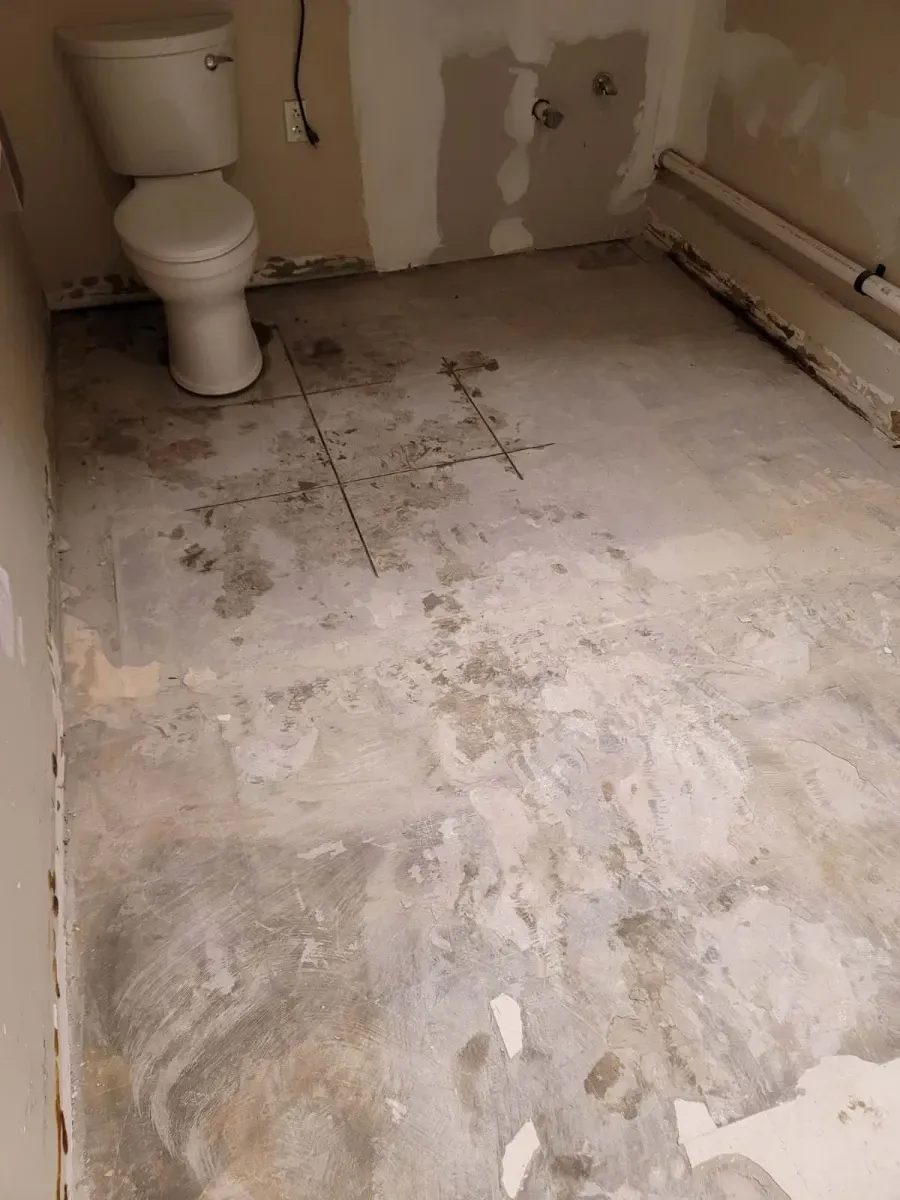 A bathroom with a toilet and bare concrete floor, walls partially covered, and a radiator along the side.