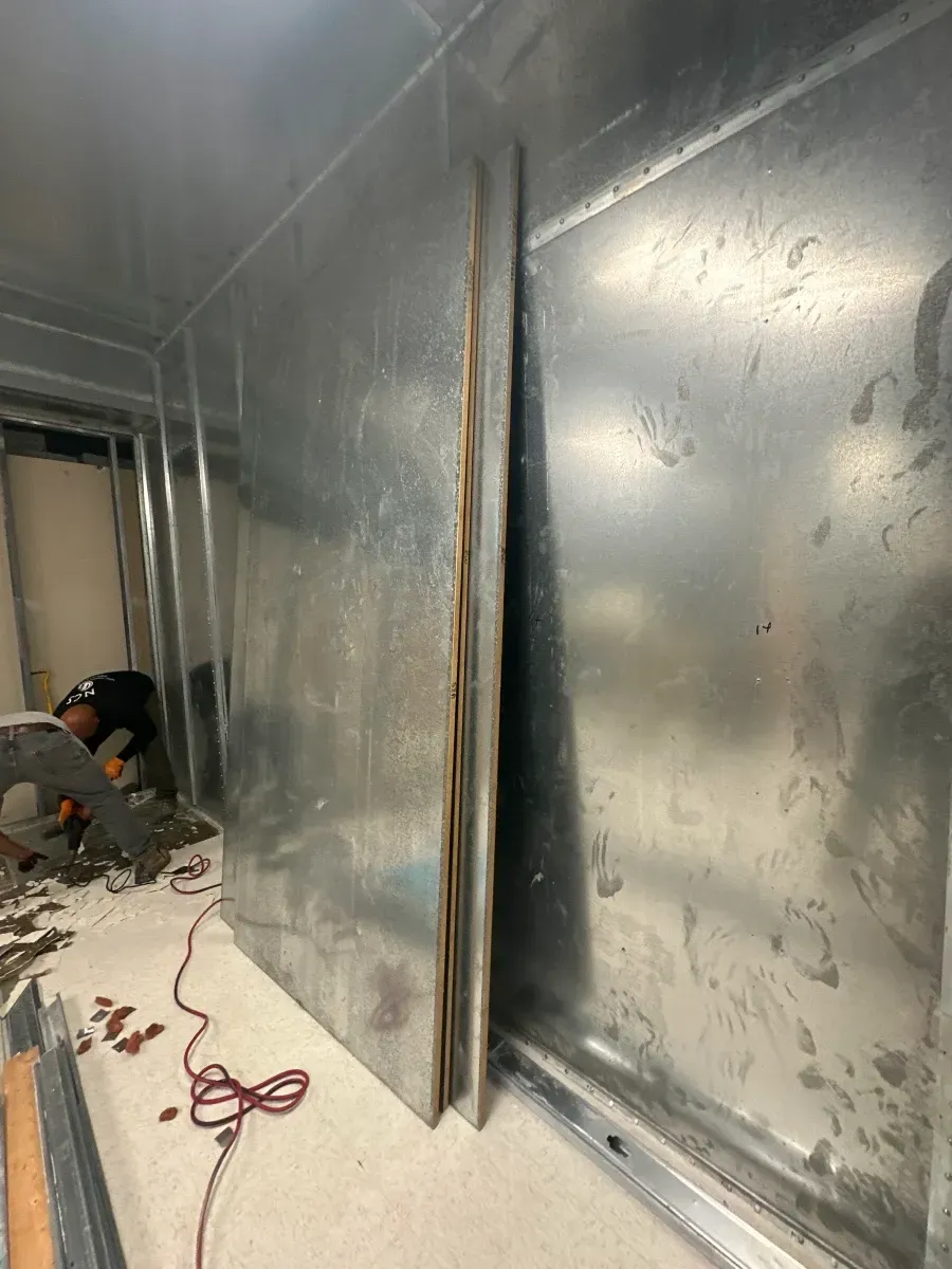 Metal sheets installed on a wall during construction; person working in the background.