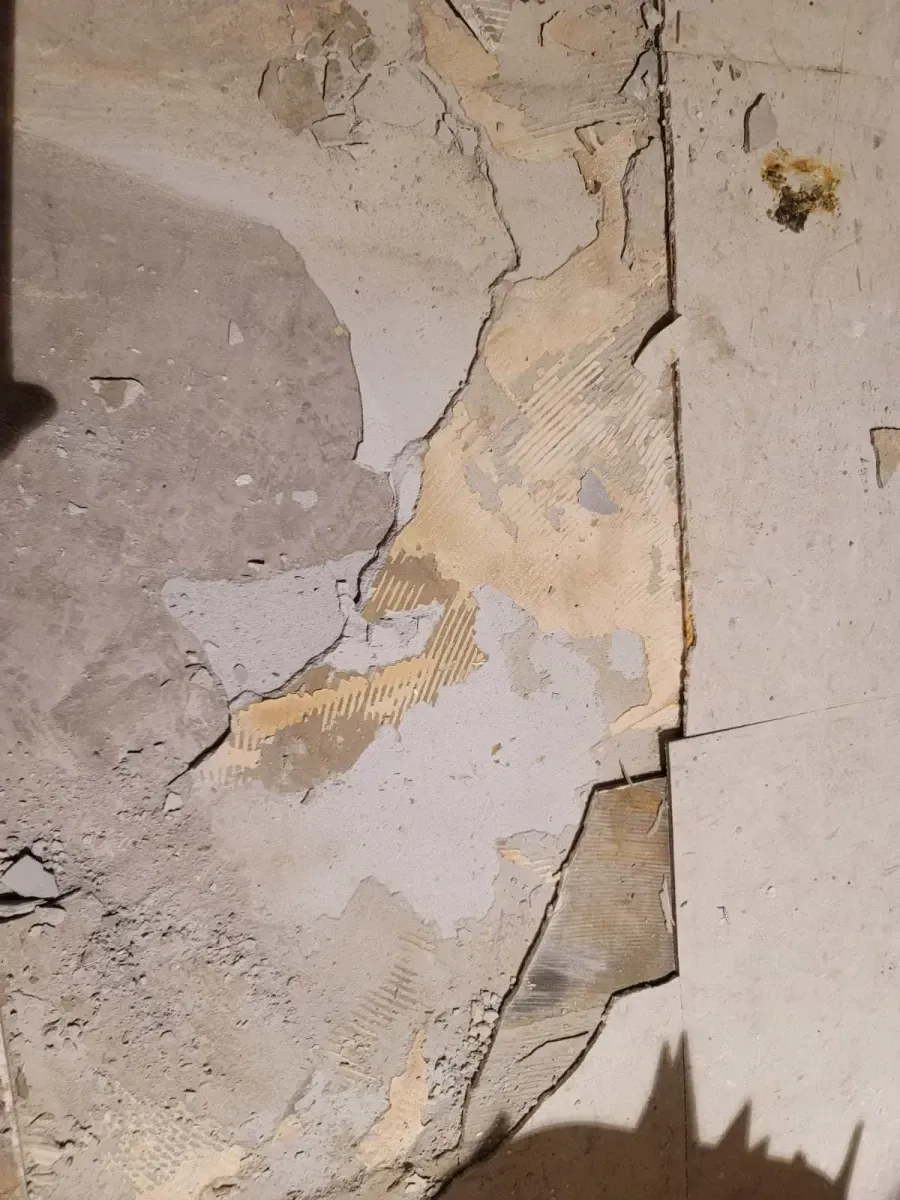 Damaged wall with torn plaster exposing layers and a vertical seam.