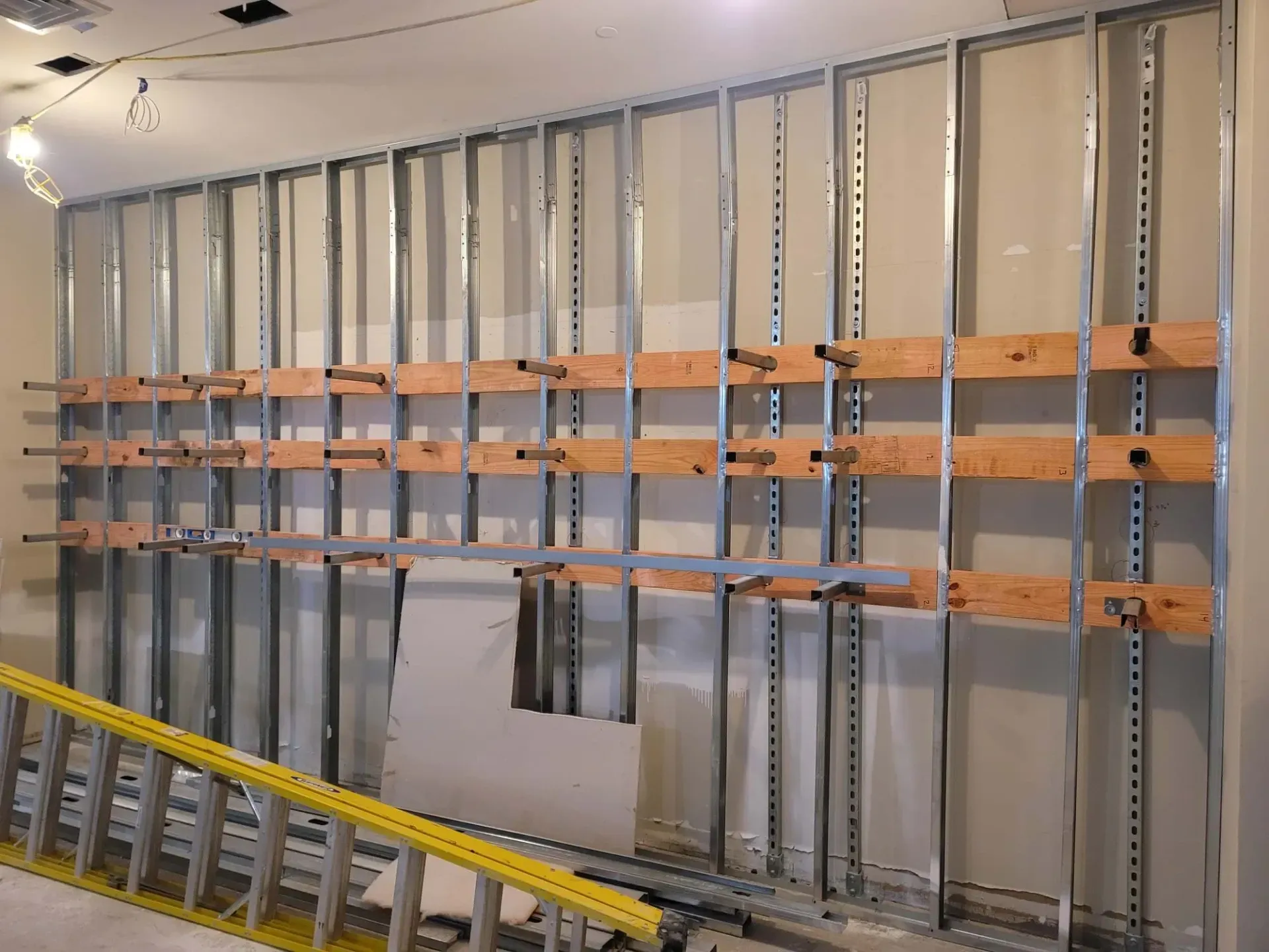 Metal studs and wood supports forming a wall frame in a room under construction.
