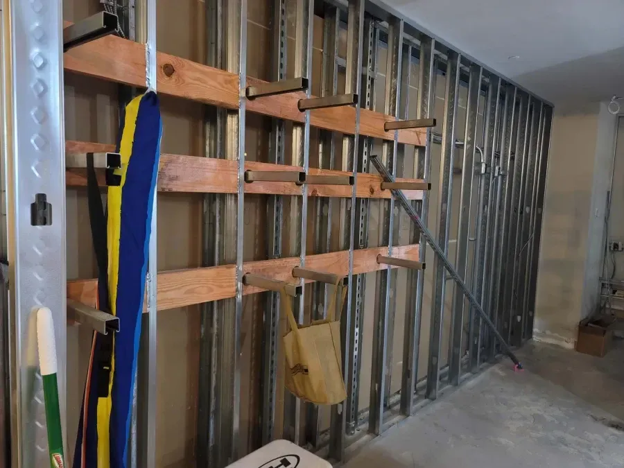 Ski and poles storage rack mounted on a steel framed wall; skis and a bag hang on the rack.