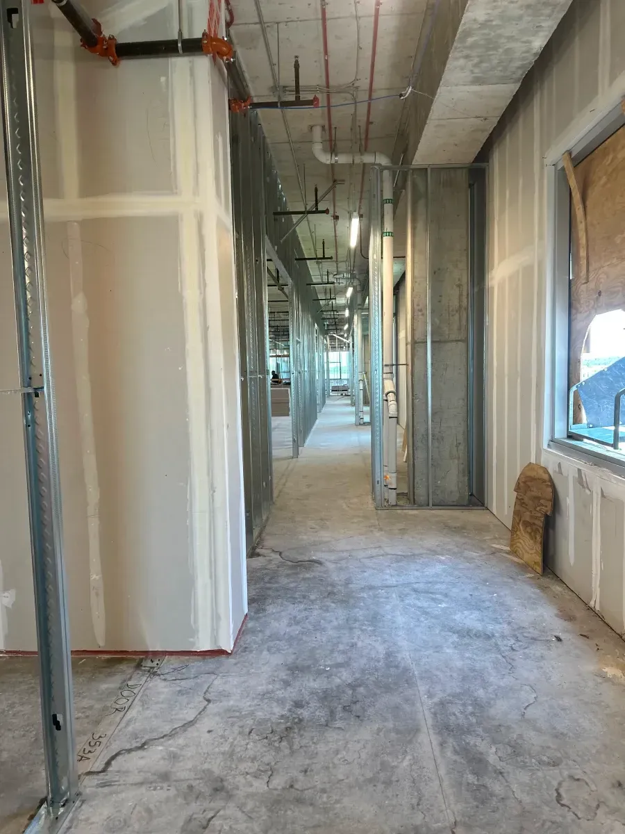 Construction hallway with exposed framework, drywall, and unfinished concrete floor.