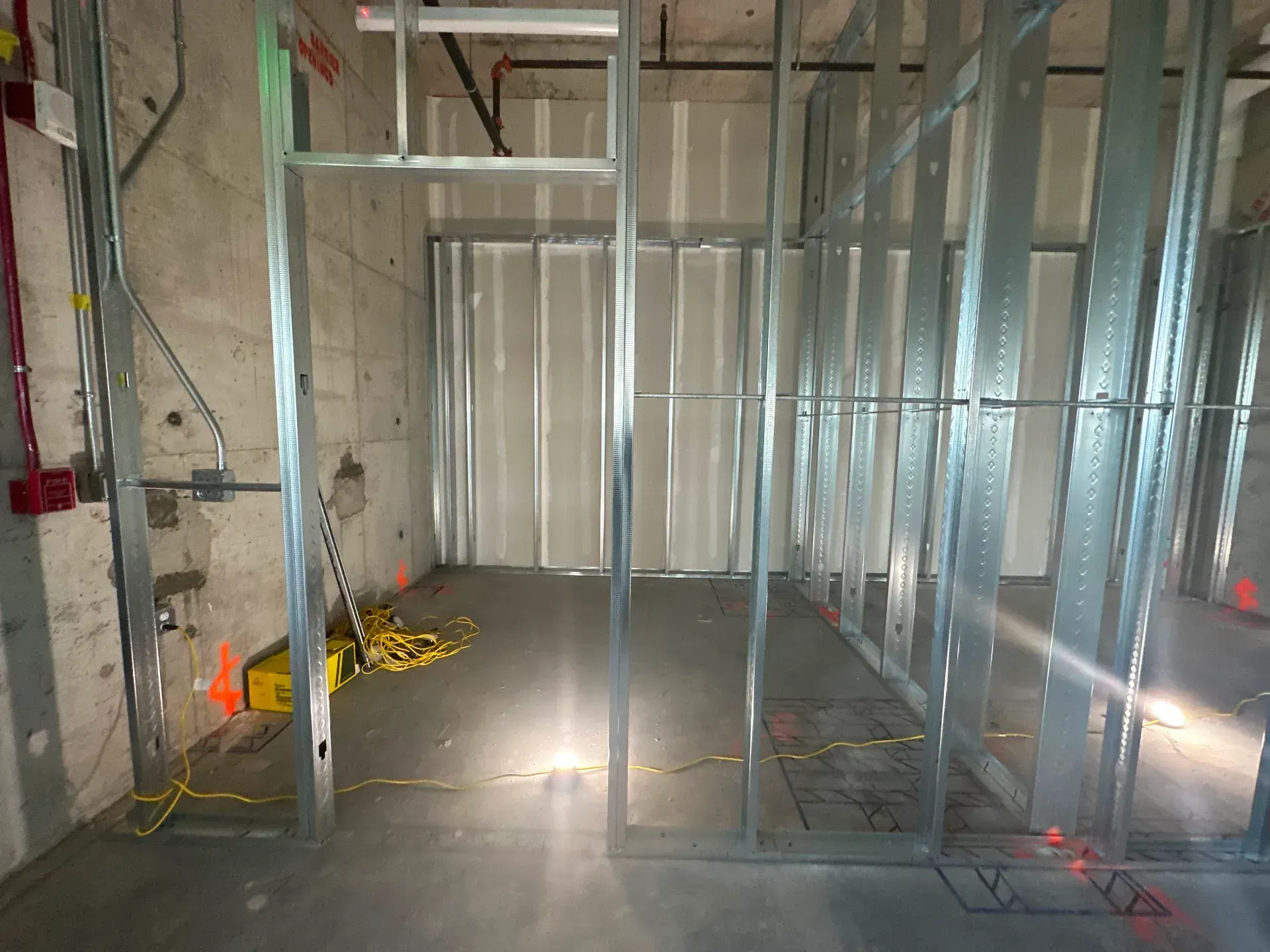 Interior of a room under construction with metal framing, concrete walls, and drywall.