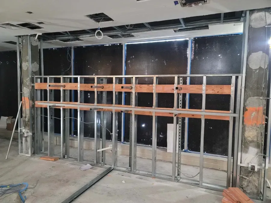 Construction site: Steel studs and wooden supports forming a wall frame. Black insulation visible.