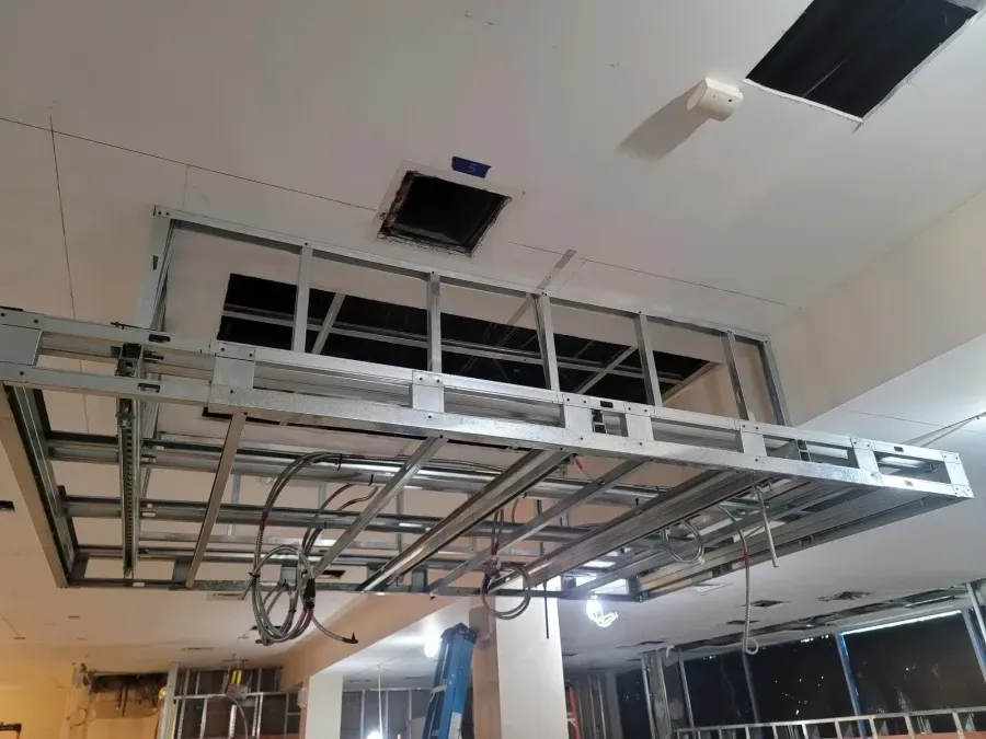 Metal framework for a ceiling feature in a building under construction, with a large square opening.