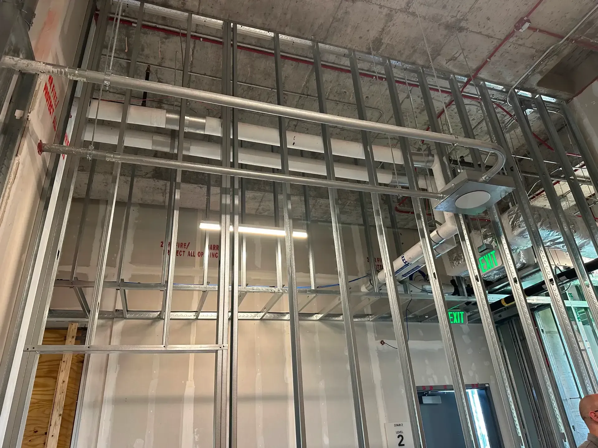Metal framing of a wall and ceiling. Electrical and plumbing components visible. Construction site.