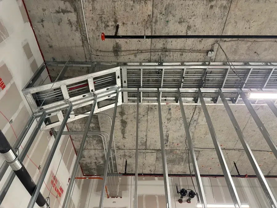 Construction site: metal framework, ductwork, and exposed concrete ceiling. Drywall is partially installed on the walls.