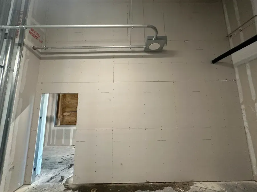 Interior wall under construction with exposed electrical conduit and doorway.