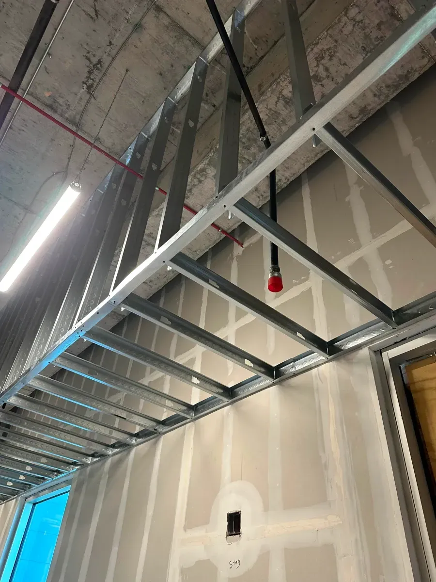 Steel framing for a suspended ceiling in a construction site. Sprinkler head and electrical outlets visible.