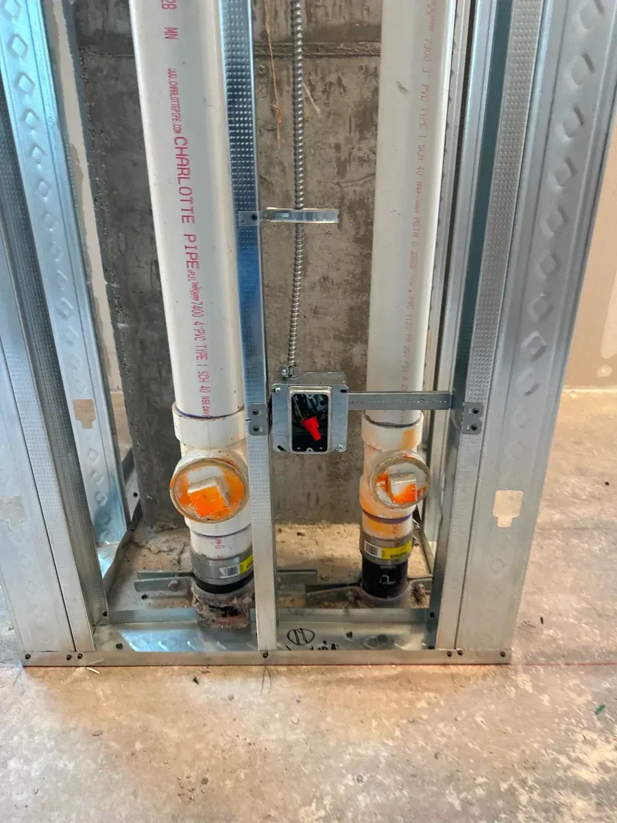 Pipes and electrical box mounted in a metal stud wall, likely for plumbing in a construction setting.
