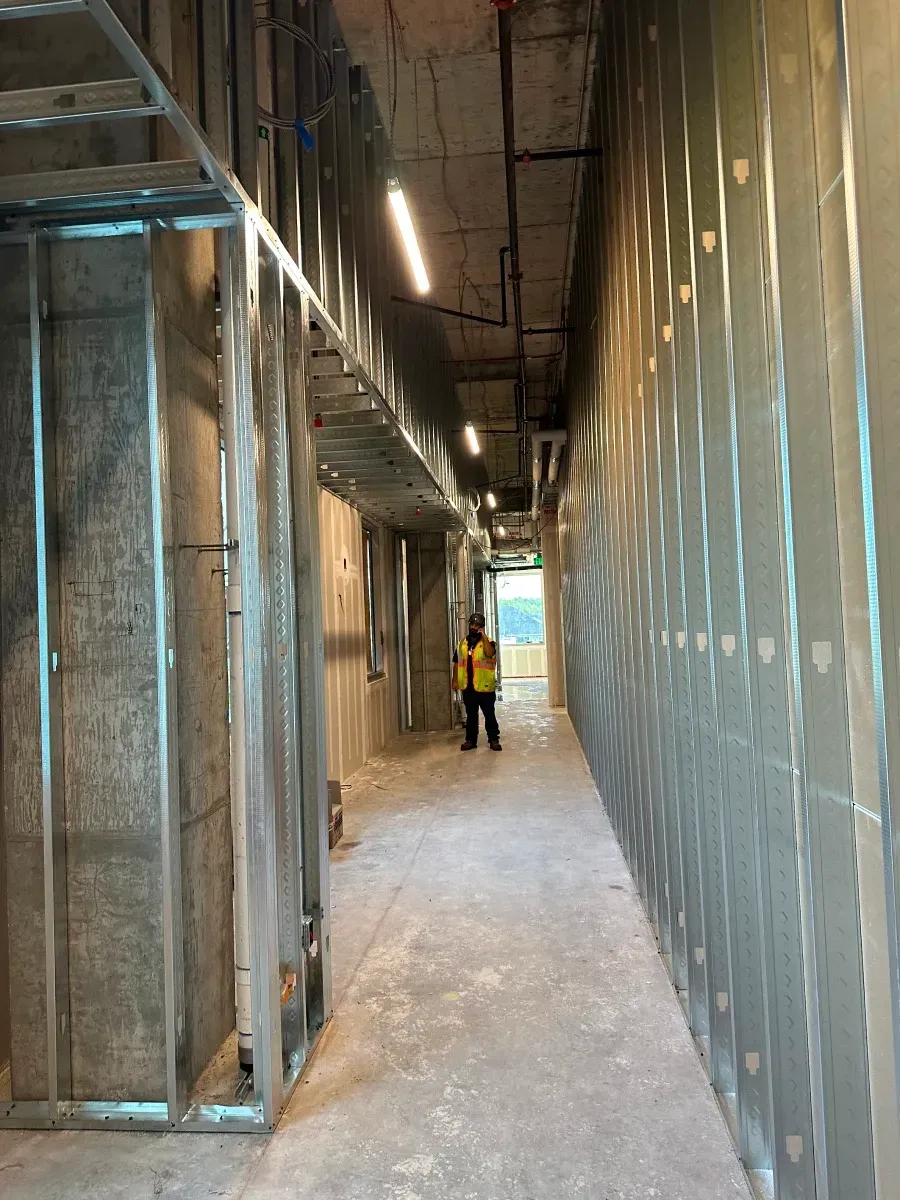Interior of a building under construction, metal frames and unfinished walls. A person in work attire stands in hallway.