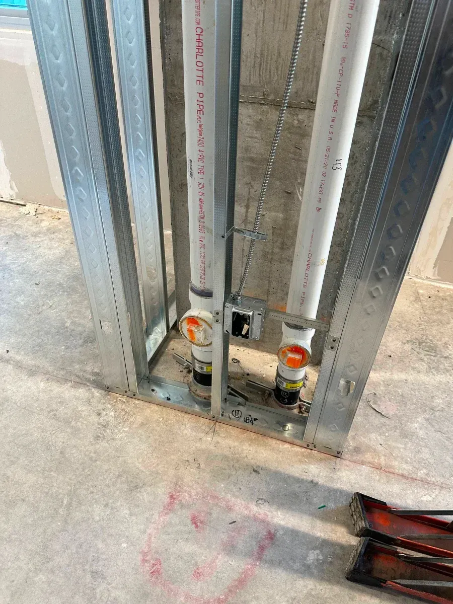 Metal frame with plumbing pipes and fittings in a concrete floor, construction site.