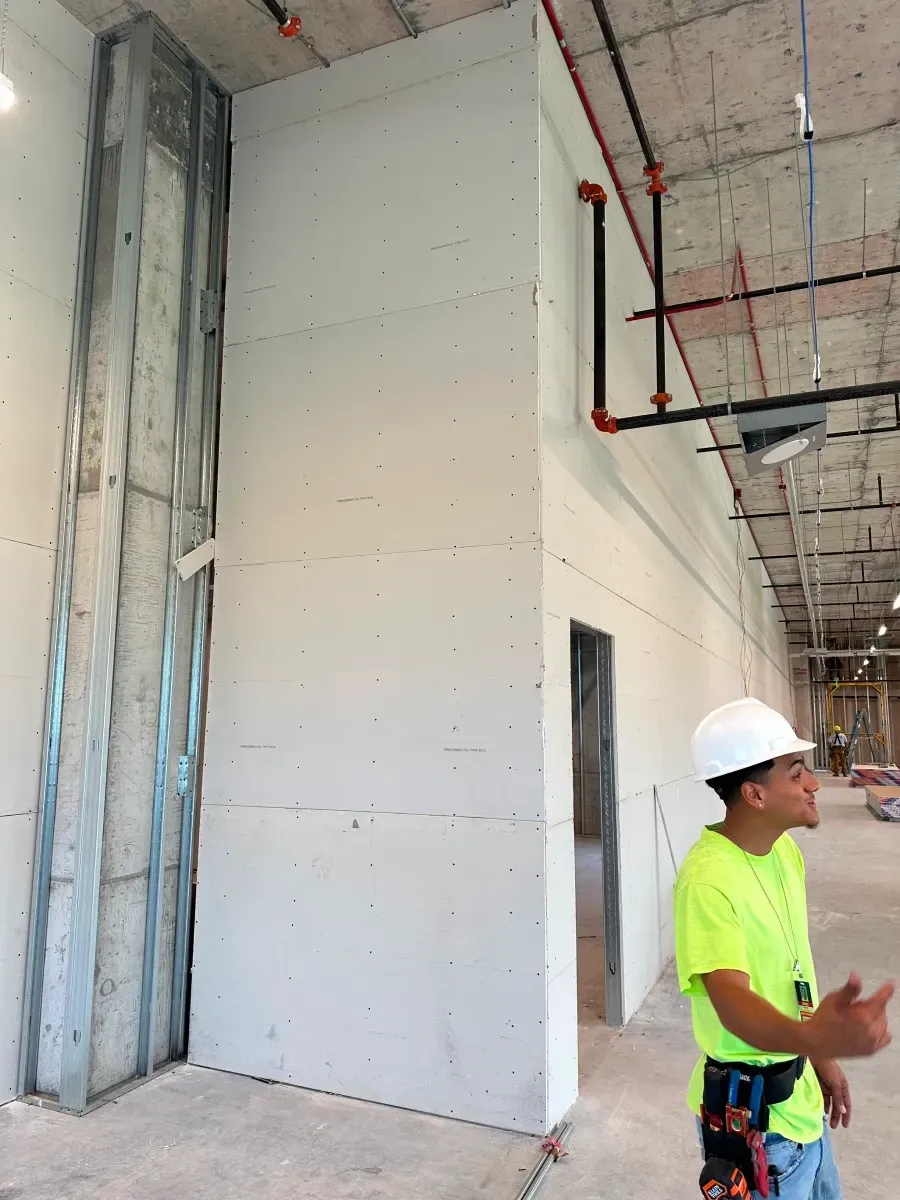 Construction worker in a hard hat, observing drywall installation in a building under construction.