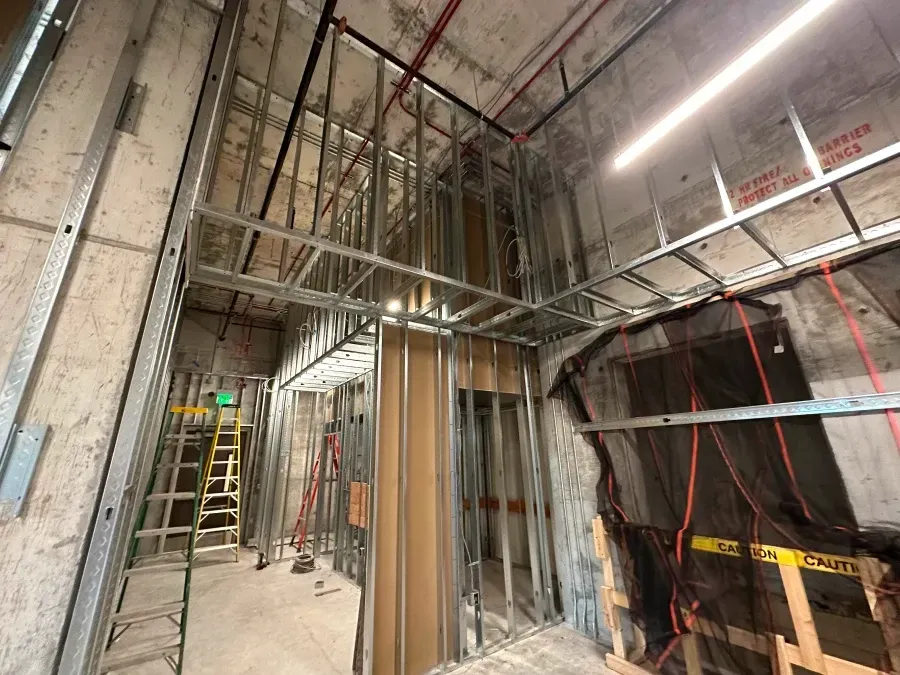 Construction site interior, steel framework for walls and ceiling, concrete, exposed wires, yellow caution tape.