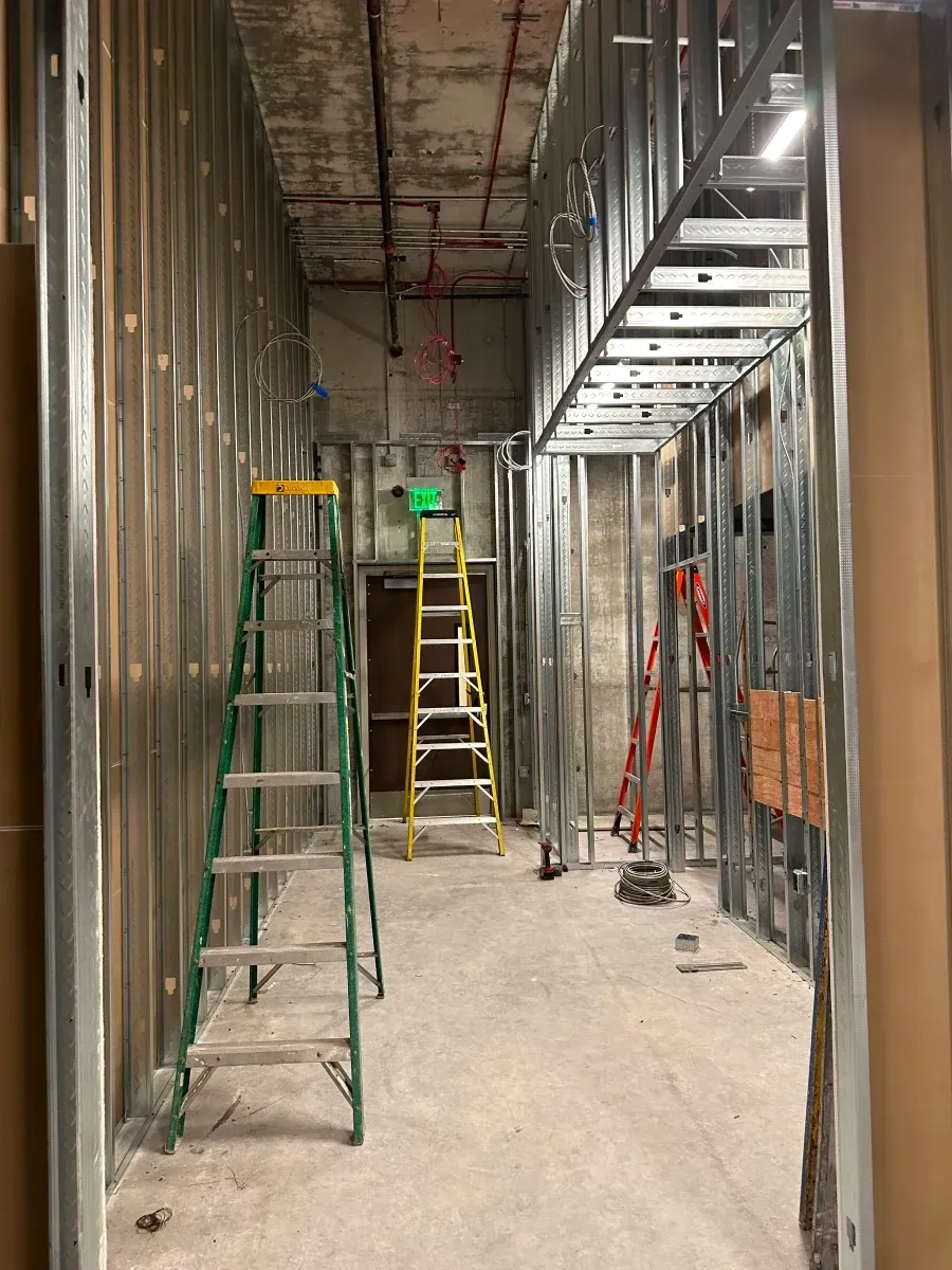 Interior construction site with metal studs, ladders, and unfinished walls.