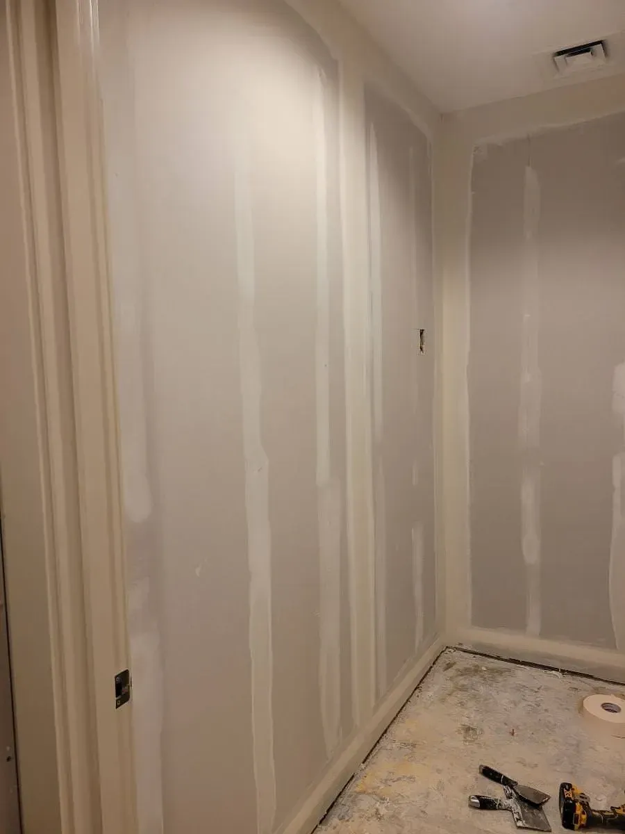 Interior room with newly installed drywall, visible seams, and trim. Floor is unfinished.