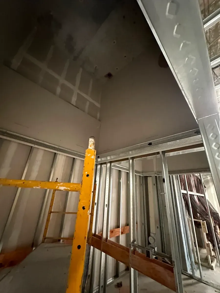 Construction site interior: drywall ceiling, metal studs, yellow scaffold.