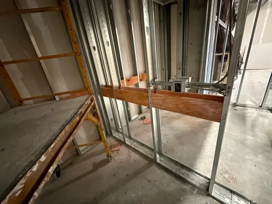 Interior construction with metal studs, wood supports, and unfinished drywall.