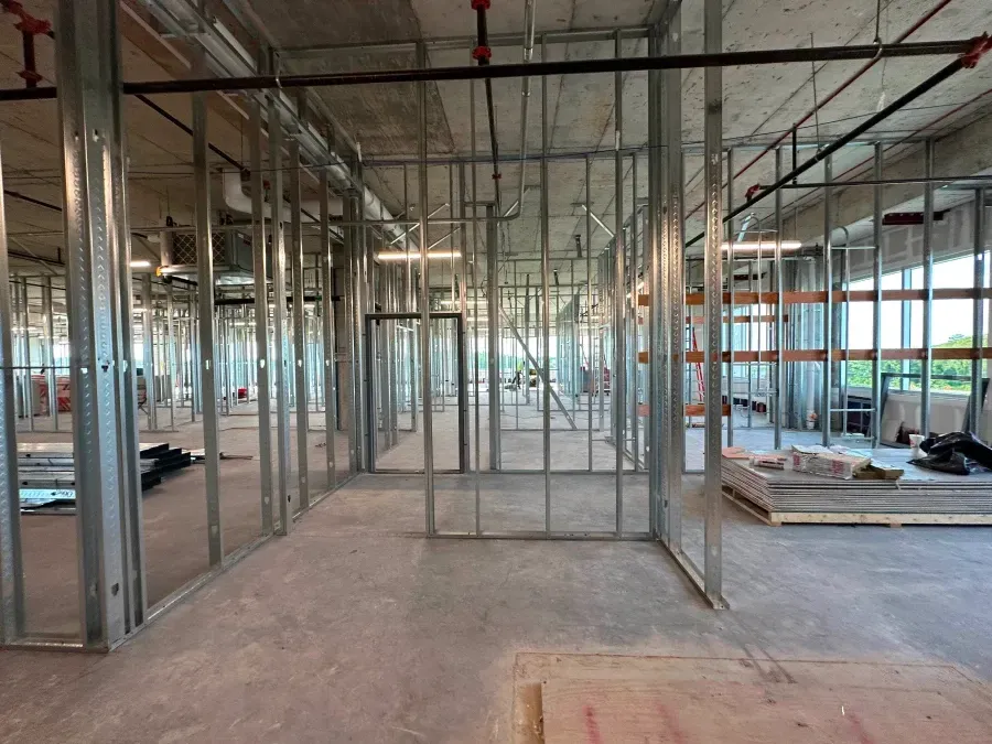 Interior construction of a building with metal stud framing, concrete floors, and exposed pipes and ducts.