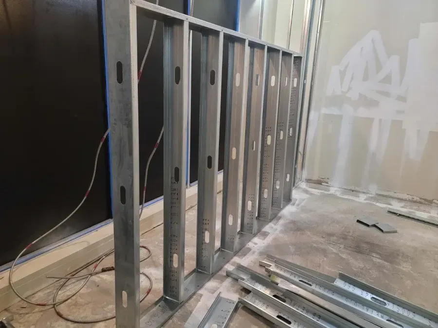 Metal studs forming a wall frame in a room under construction, wires visible.
