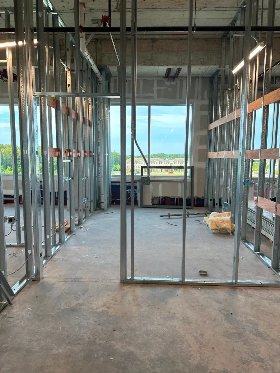 Interior construction site with metal studs forming walls; window with outdoor view in background.