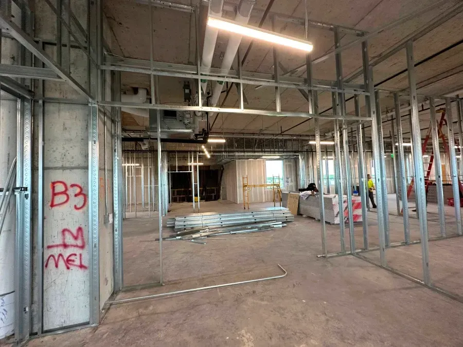 Interior view of a building under construction. Metal framing outlines walls and doorways in an open space.