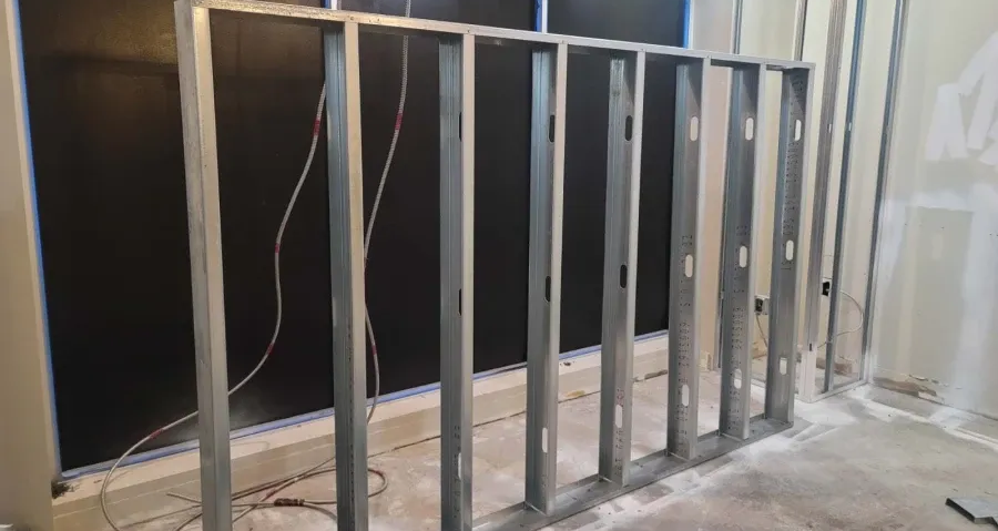 Metal stud framing for a wall, with electrical wiring visible, against a dark backing.