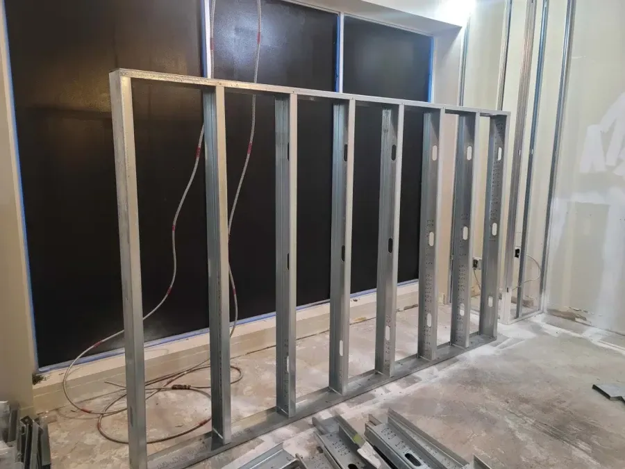 Metal stud framing for a wall under construction, against black insulation; interior setting.