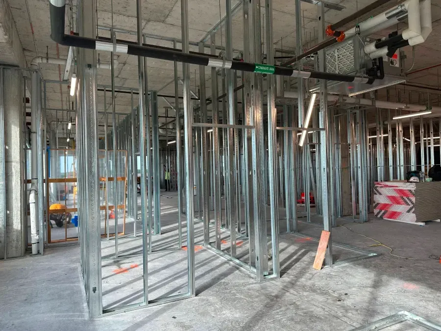 Interior of a building under construction, metal stud framing for walls and ceiling, pipes.