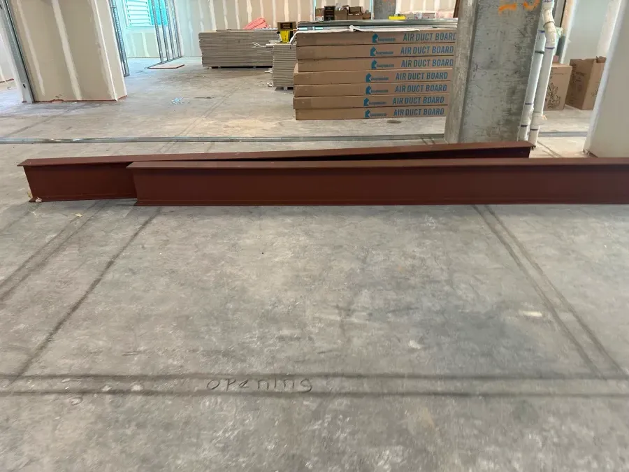 Two long, rusty-red steel beams on a gray concrete floor in a construction site.