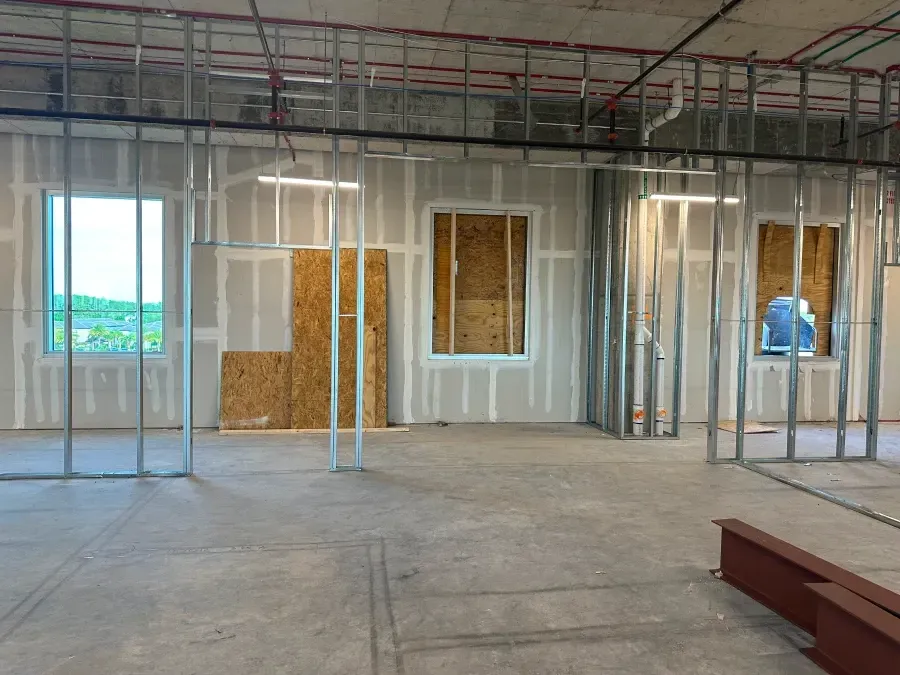 Interior of a building under construction. Metal framing and drywall define the walls, windows and doorways. Concrete floor.