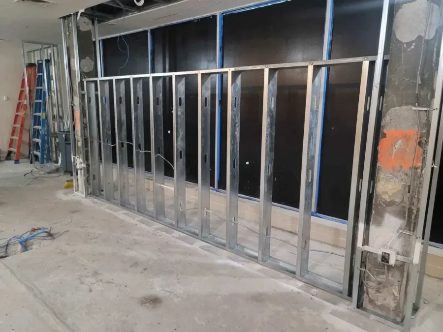 Metal stud framing for a wall in a construction zone. Electrical wires visible. Concrete floor and dark background.