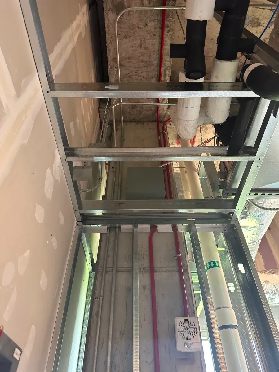 Metal frame ceiling construction with pipes and wiring visible.