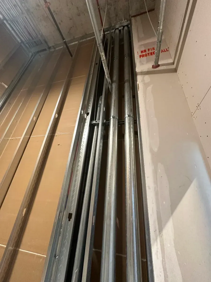 Metal conduits and framing inside a wall cavity.  Drywall and concrete ceiling visible.