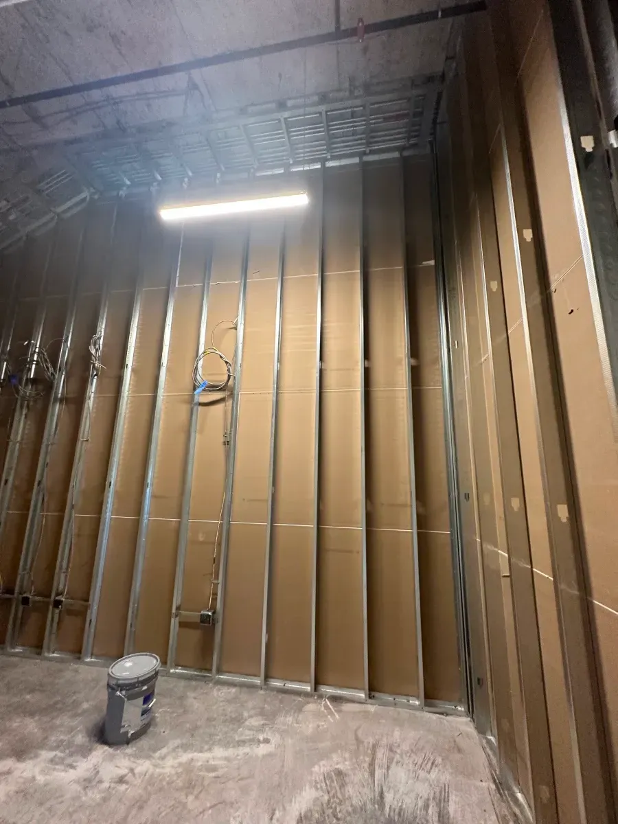 Interior of a room with metal studs and large cardboard panels covering the walls. A light fixture is mounted on the ceiling.