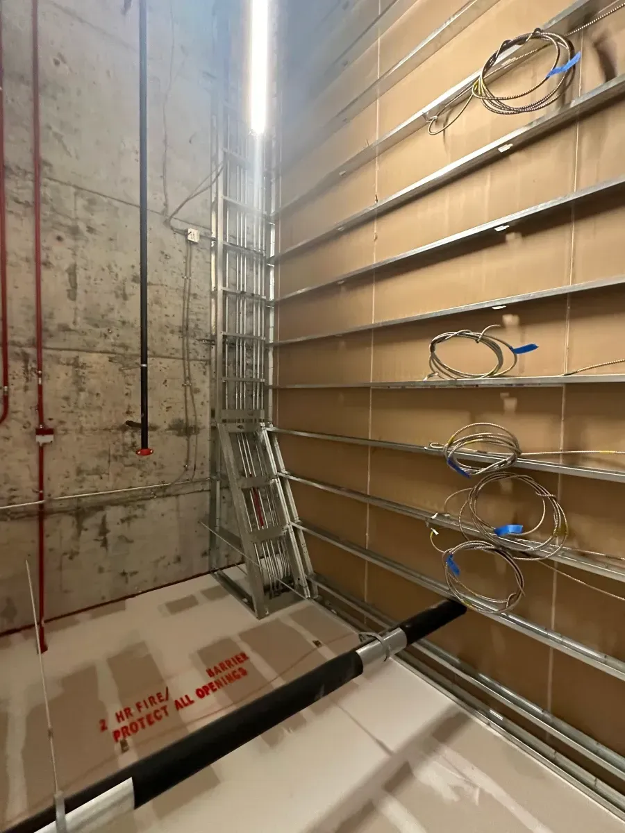 Interior construction site with metal framing, exposed pipes, and a ladder.