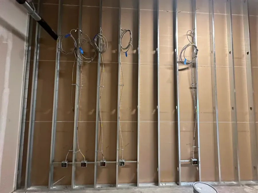 Interior wall under construction with metal studs, wiring, and electrical boxes.