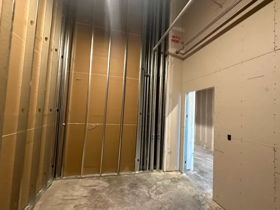 Interior construction site with metal studs, insulation, and drywall. Doorway leads to another room.