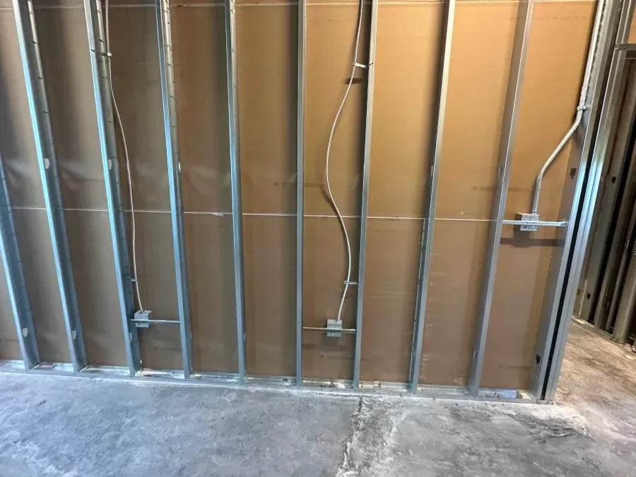 Metal studs and drywall with electrical conduit and junction boxes in a partially constructed room.